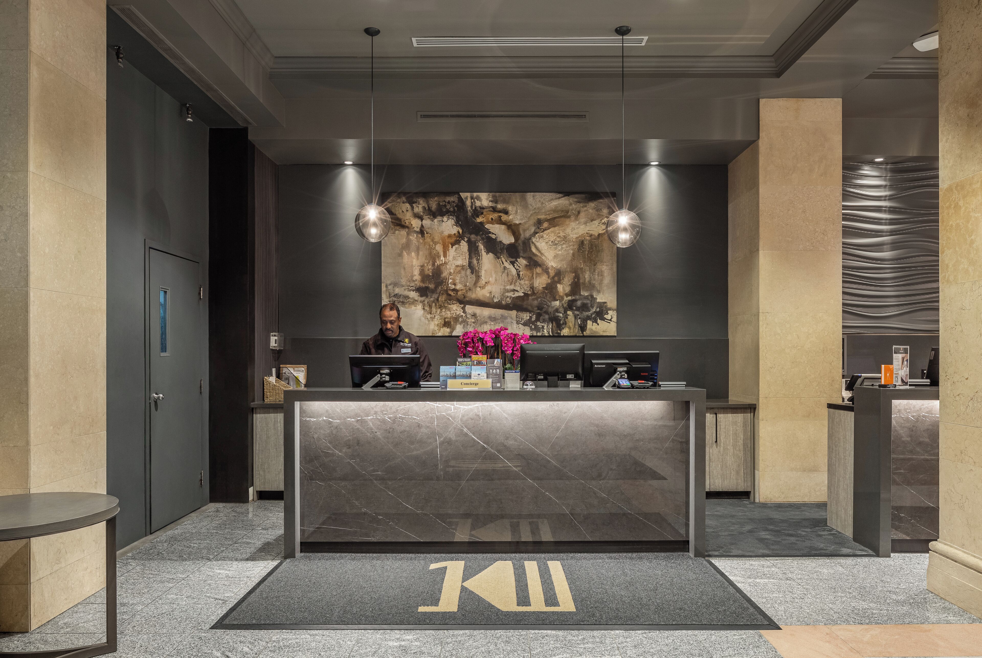 A reception desk with a modern design, a large abstract painting on the wall, and a logo on the floor.
