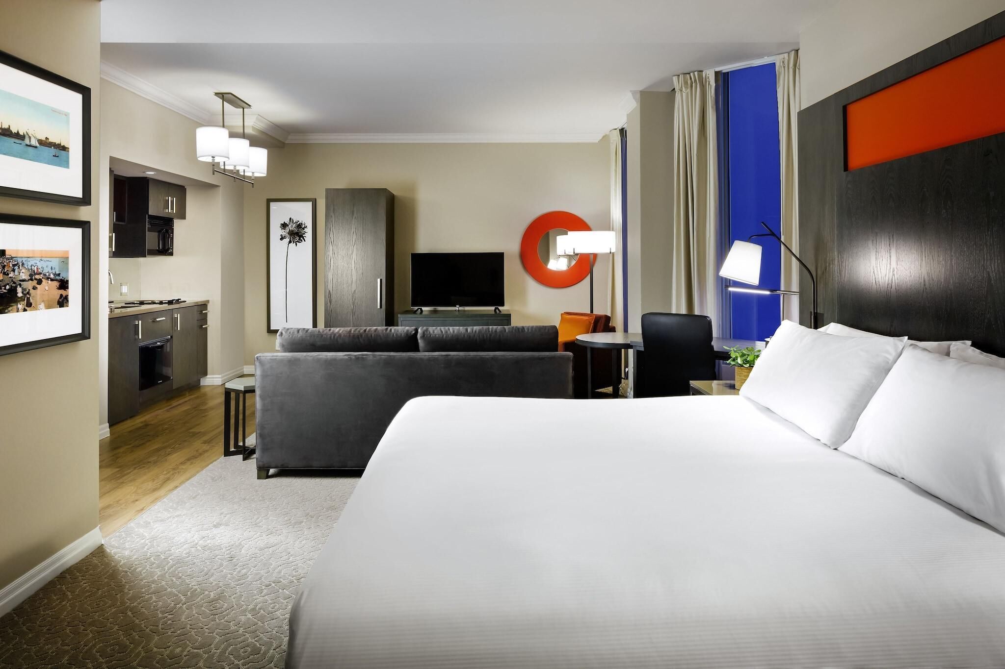 A hotel room with a large bed, a sofa, a TV, a desk, and a kitchen area.