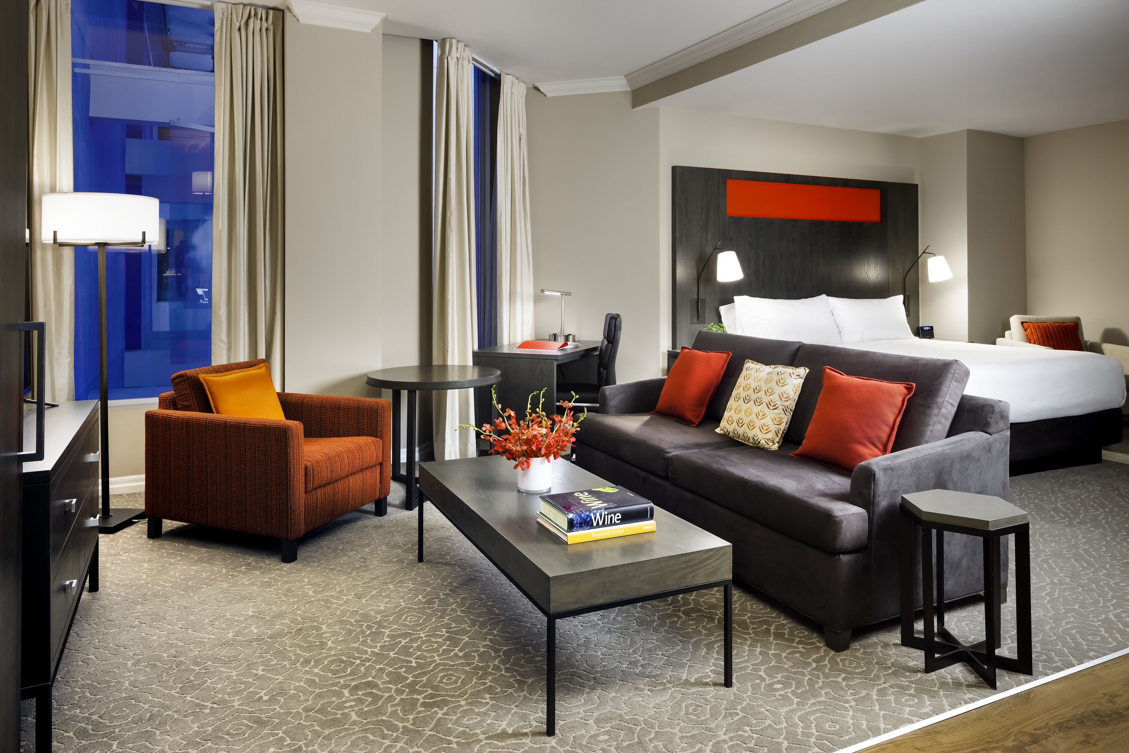 A hotel room with a bed, a sofa, a coffee table, a chair, and a small table.