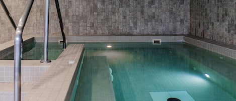 Una piscina interior con paredes de azulejos y una escalera de metal.