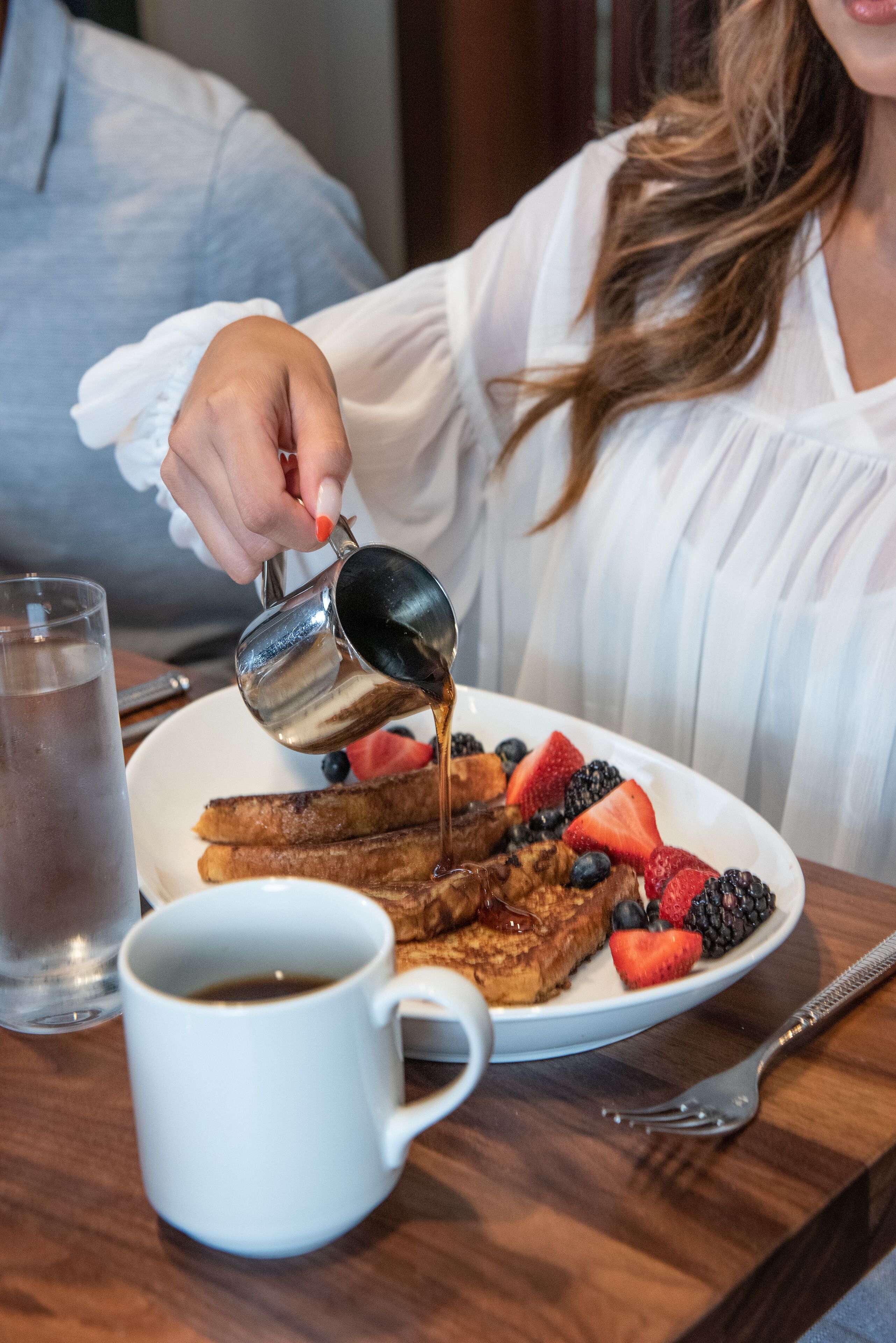Fransk toast med bær og sirup, et glas vand og en kop kaffe på et træbord.