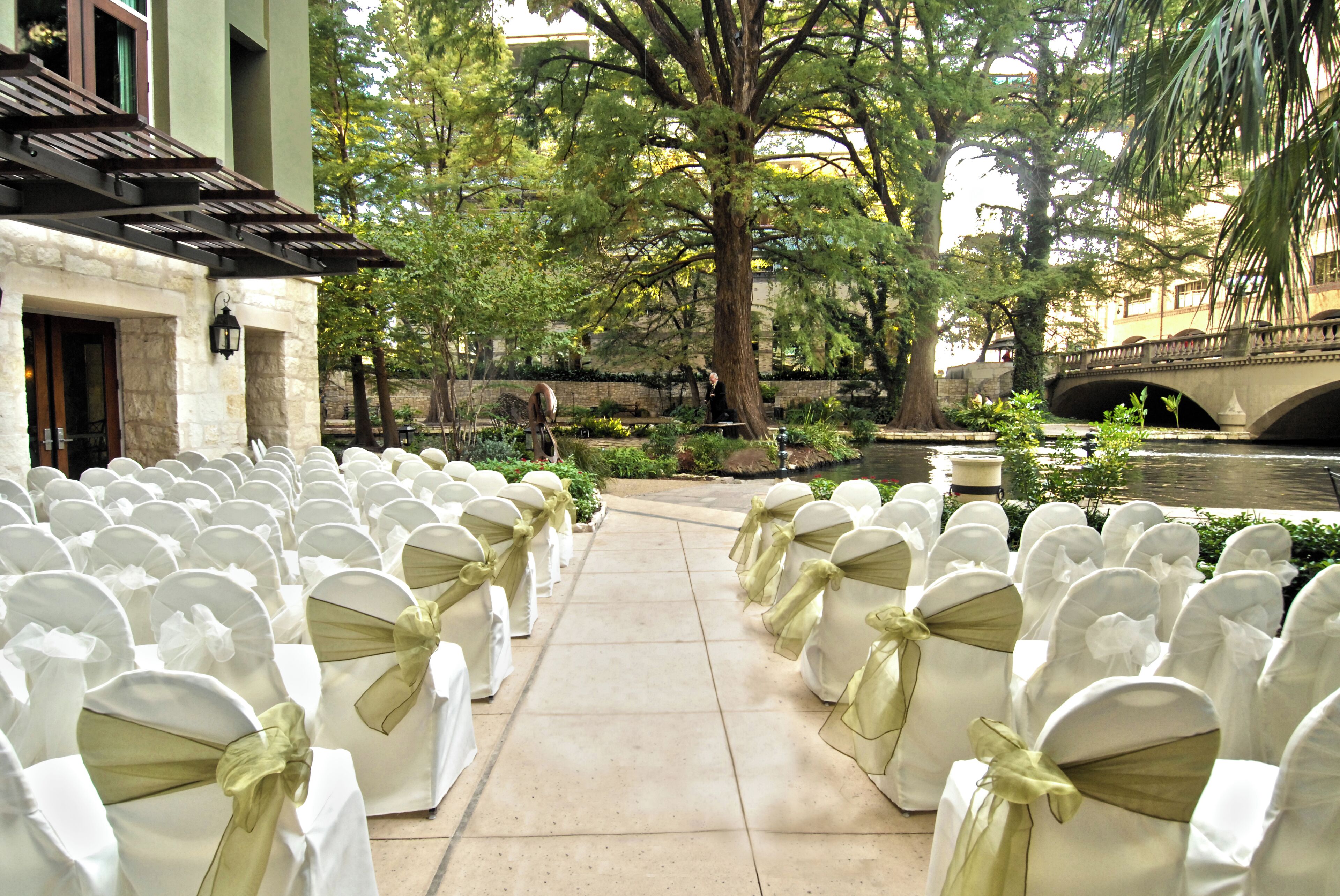 Rows of white chairs with green sashes, a stone building, and a bridge over a water body.