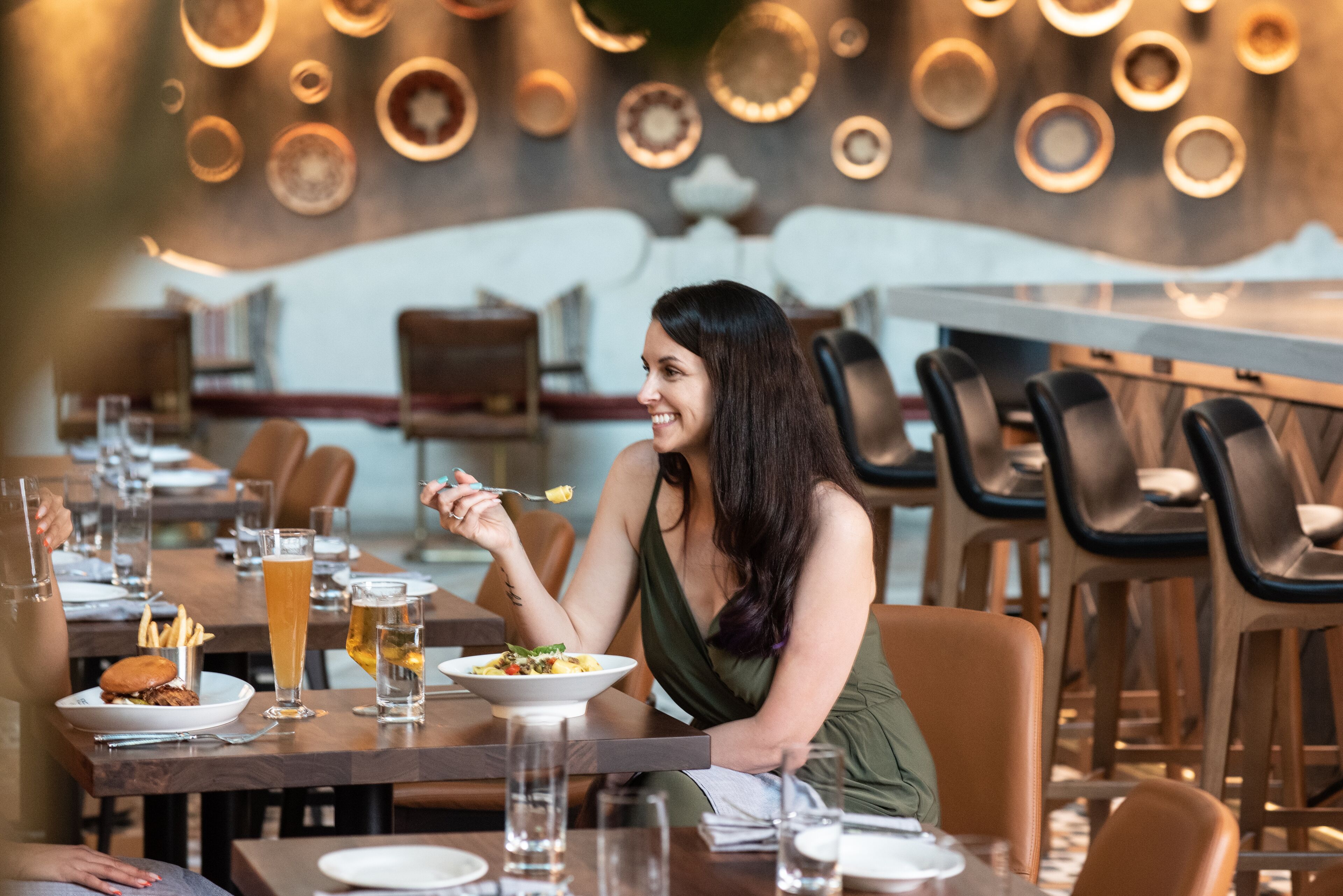 A woman dining at a restaurant with a high table, plates of food, and drinks.