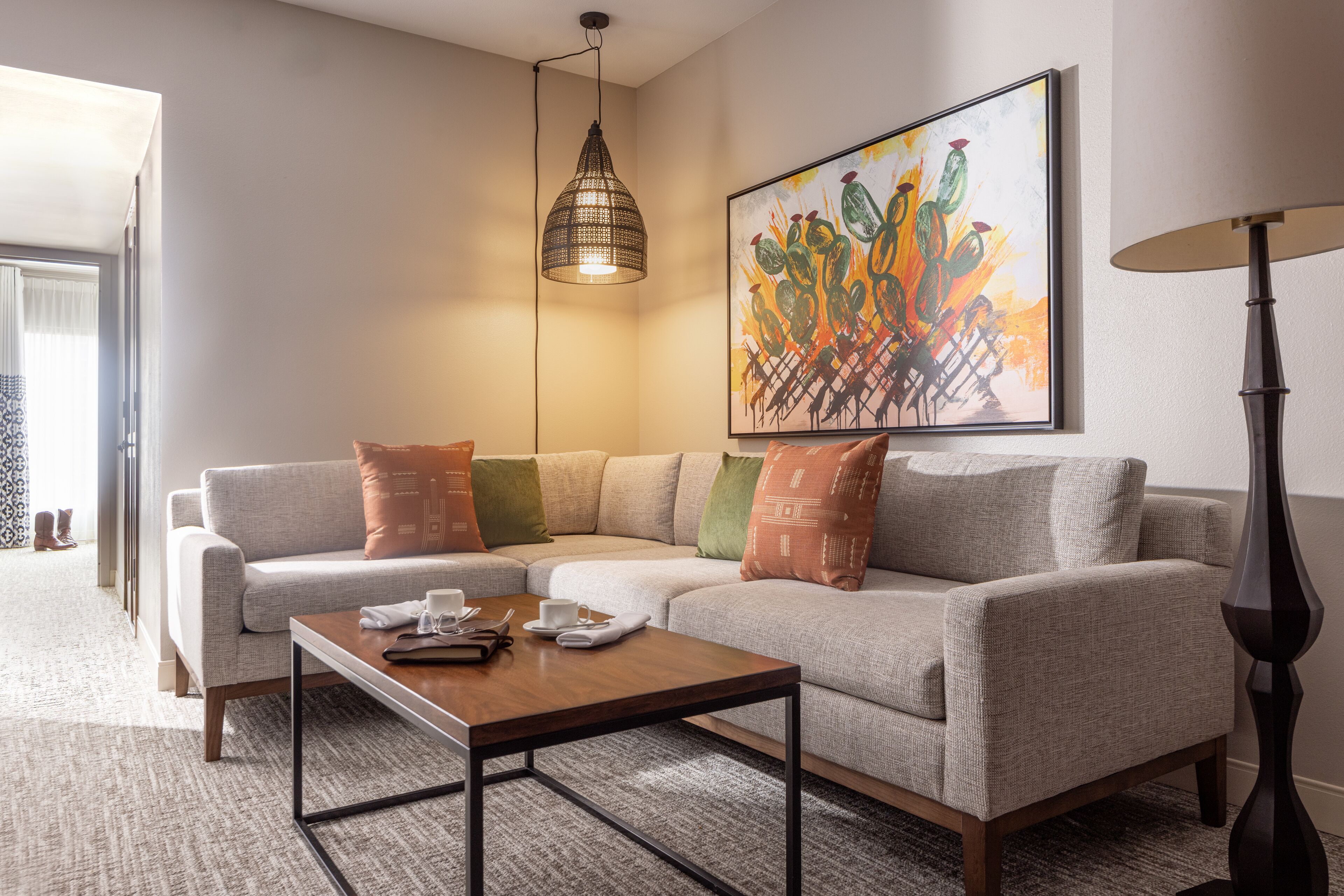 A modern living room with a sectional sofa, a coffee table, a pendant light, and a painting on the wall.