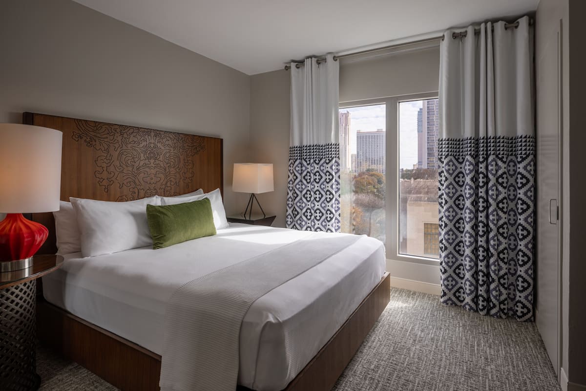 Une chambre d’hôtel avec un grand lit, deux lampes de chevet, un rideau à motifs et une vue sur la ville.