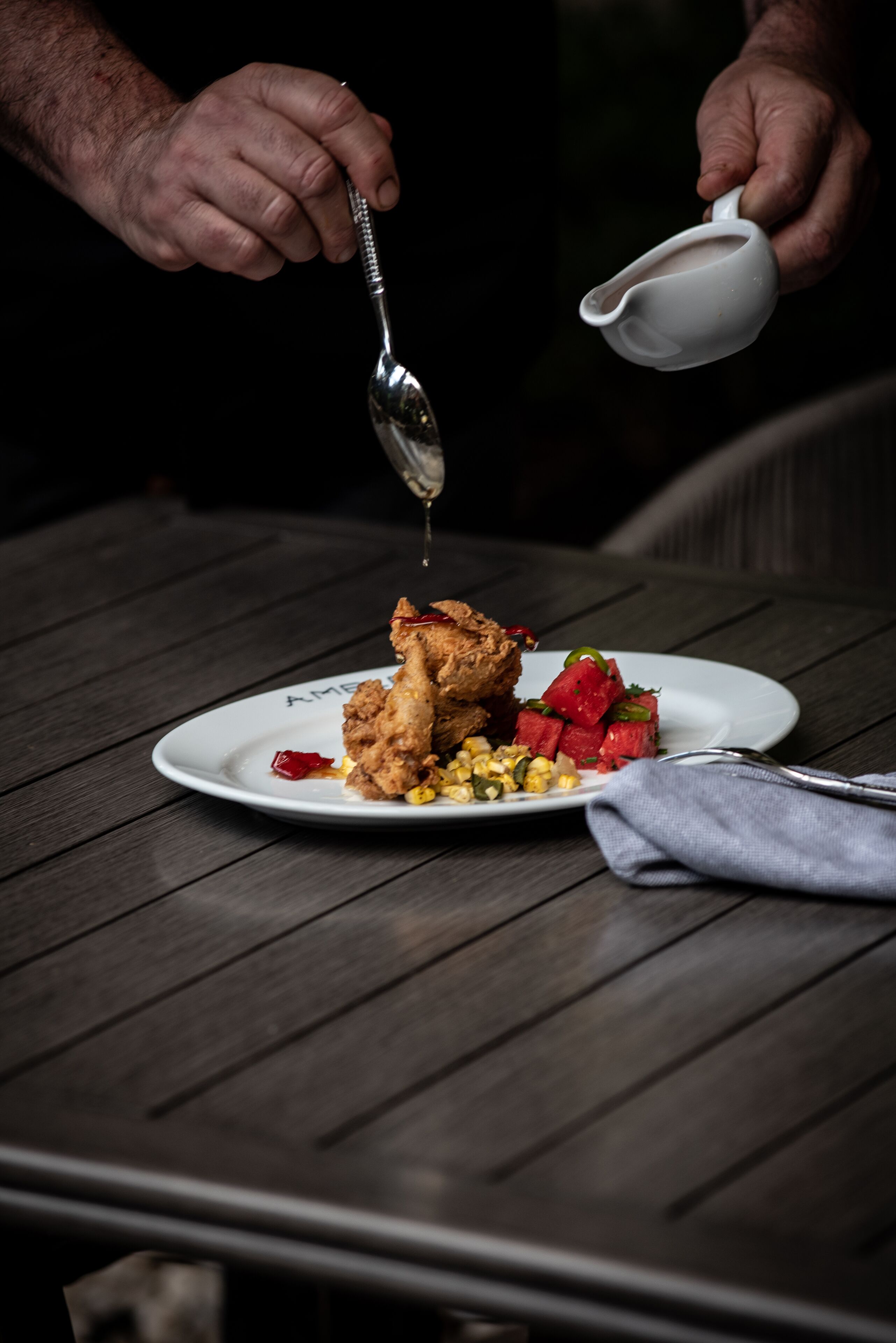 Una persona sirviendo salsa sobre pollo frito y verduras en un plato.