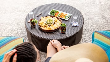 A round wicker table with a plate of vegetables, a bowl of dip, and two glasses of water.