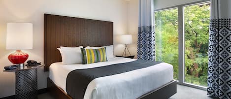 Una habitación de hotel con una cama grande, dos mesitas de noche, una lámpara roja y vistas a zonas verdes por la ventana.