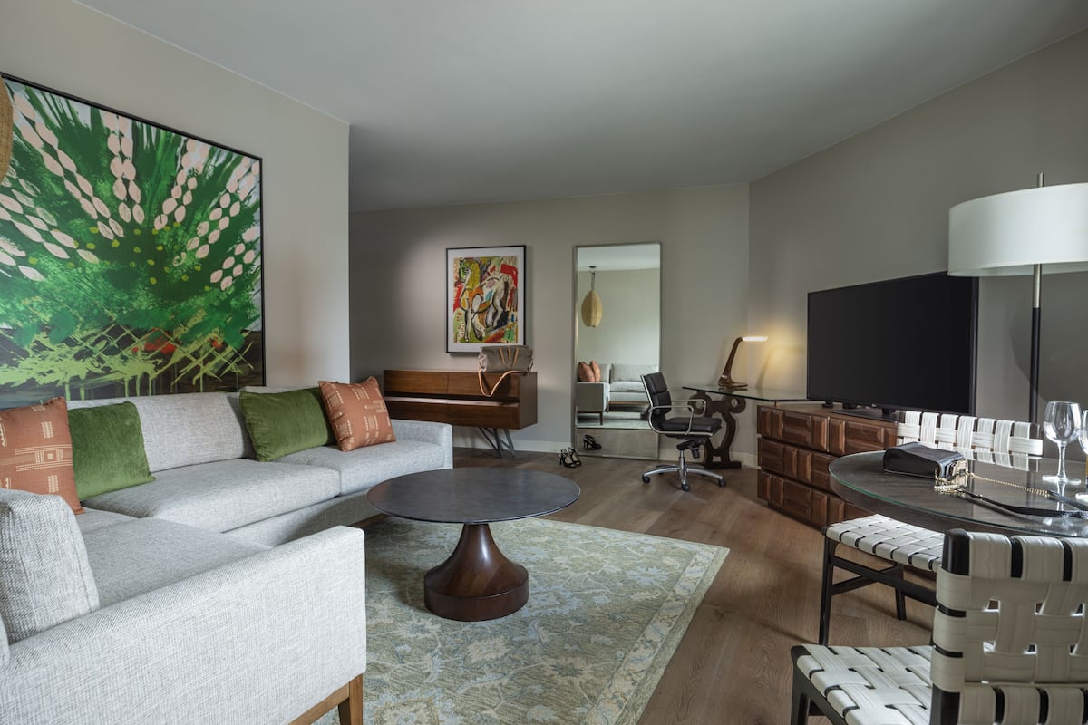 Un salon moderne avec un canapé gris, une table basse ronde, une table à manger avec des chaises, un téléviseur et des œuvres d’art accrochées aux murs.