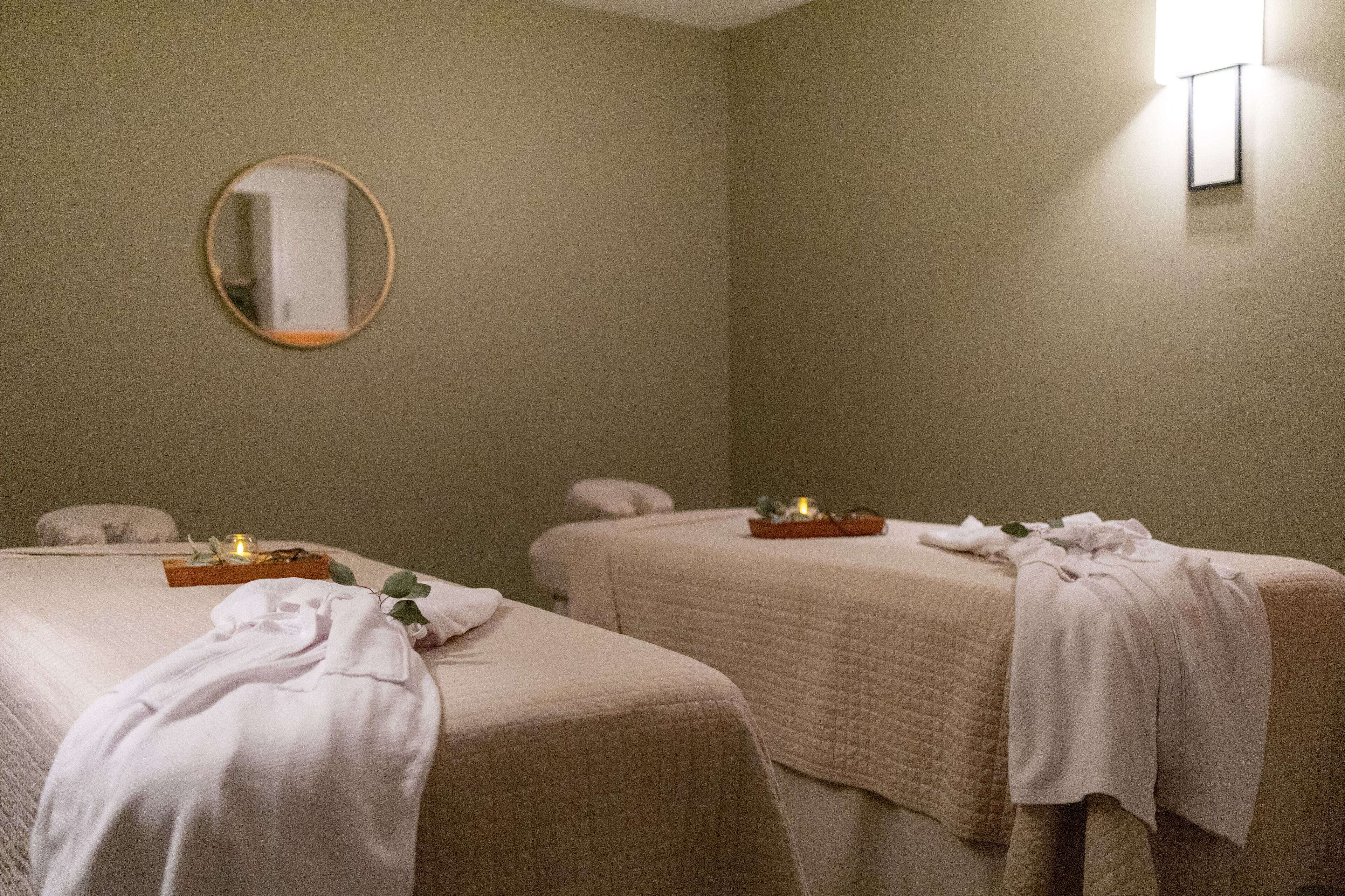 A hotel room with two beds, a mirror, and a small table with a candle.
