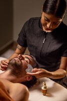A person receiving a facial treatment with a facial mask and a bottle of oil on a table.
