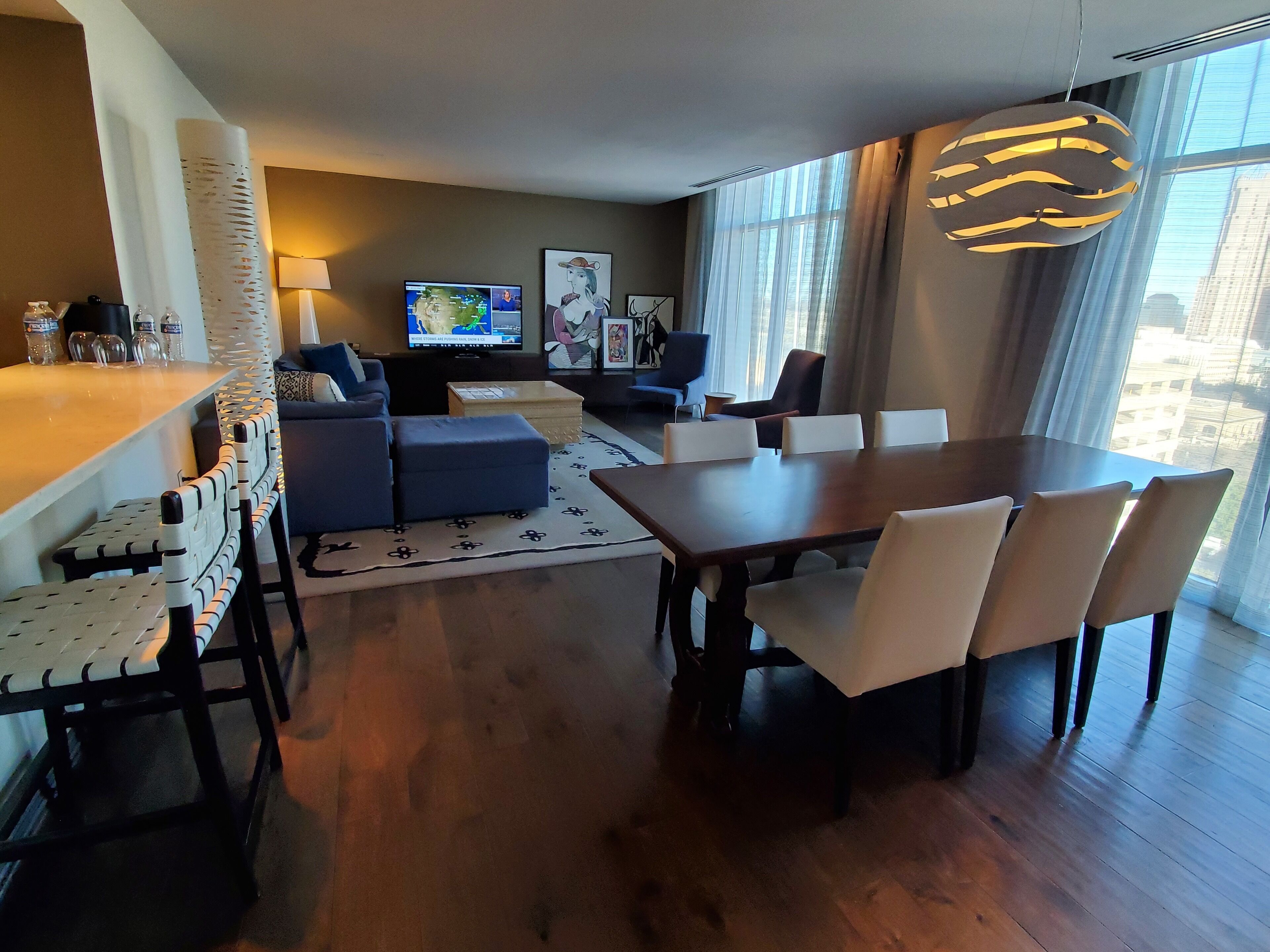 Una sala de estar moderna con comedor, televisor y un amplio ventanal con vista a la ciudad.