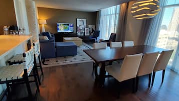Una sala de estar moderna con comedor, televisor y un amplio ventanal con vista a la ciudad.