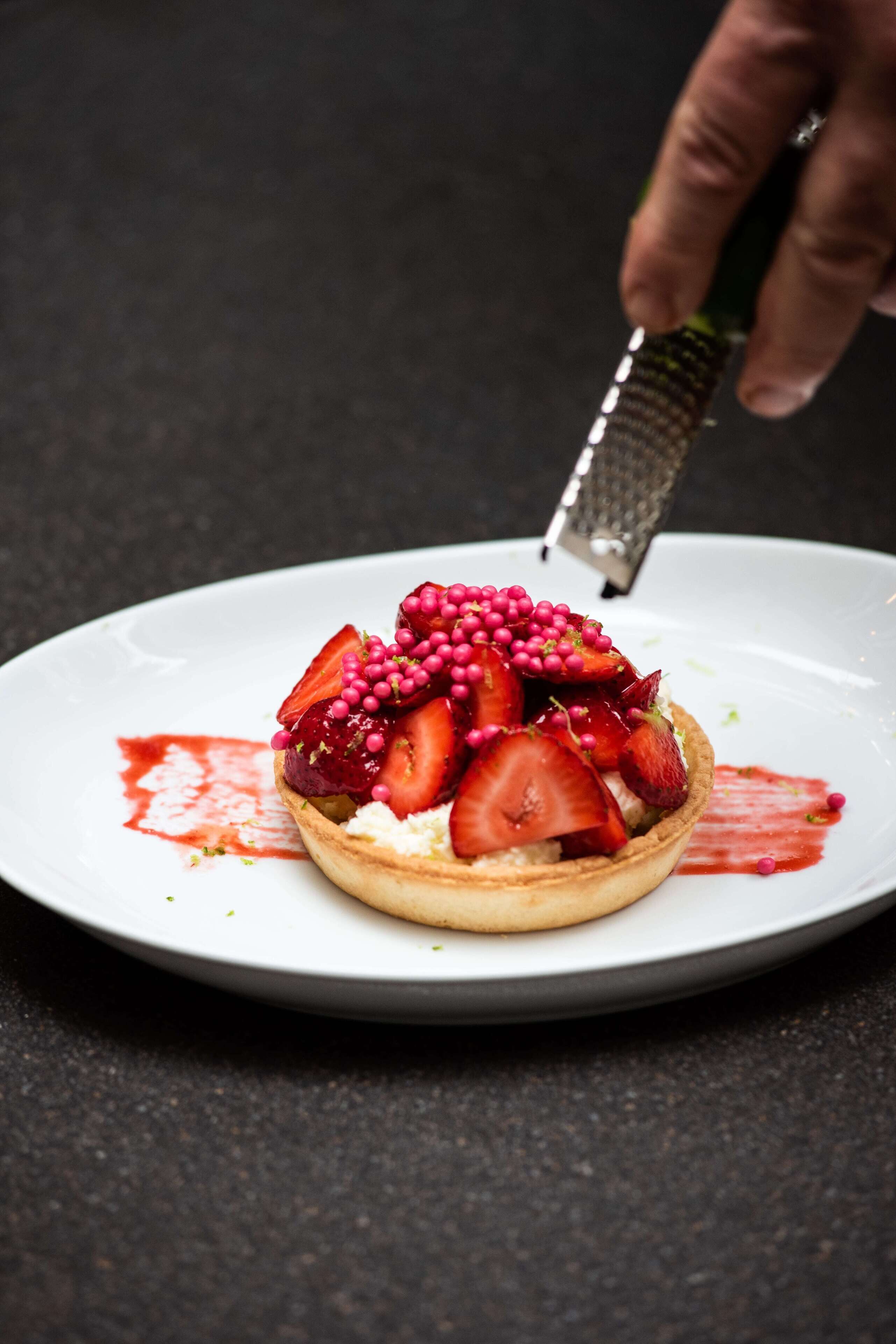 A dessert on a plate with strawberries and berries, and a hand grating something on top.