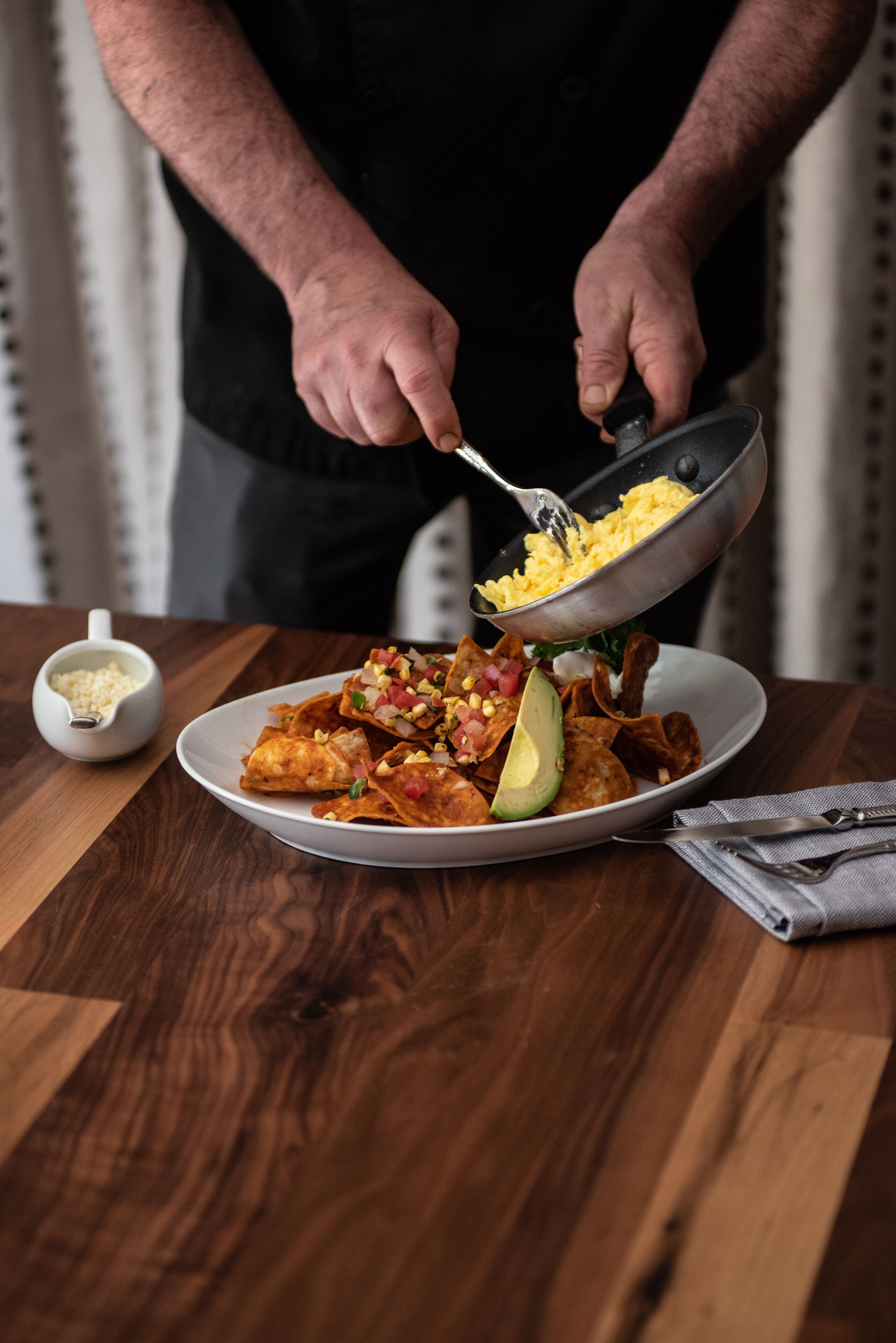 Una persona sirve un plato de comida con un cuenco de maíz y un pequeño recipiente con queso.