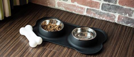 A black pet feeding station with two bowls on a wooden floor.