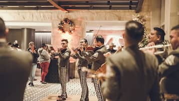 A group of musicians performing in a room with a patterned floor and a decorative wreath on the wall.