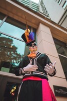 Una persona con chaqueta negra con detalles blancos, un fajo rojo y un sombrero alto y colorido.