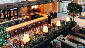 Een open hotel lobby met meerdere niveaus, een bar, zitplaatsen en een zichtbaar 'AMBULER'-bord.
