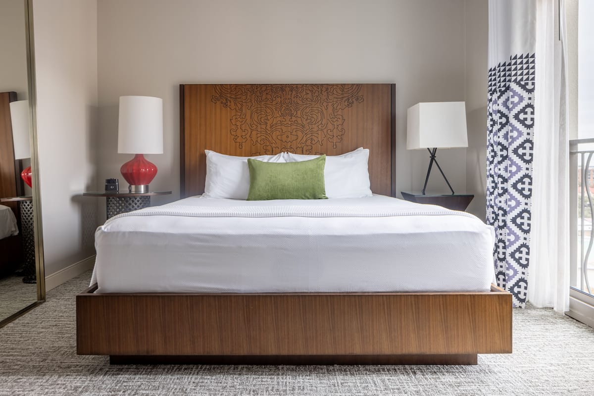 Une chambre d’hôtel avec un grand lit, deux lampes de chevet, une tête de lit en bois et un rideau à motifs.