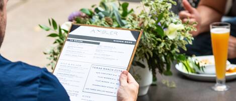 A person holding a menu at an outdoor table with a drink and a potted plant.