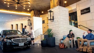 A modern hotel lobby with a black car, a staircase, and a seating area with guests.
