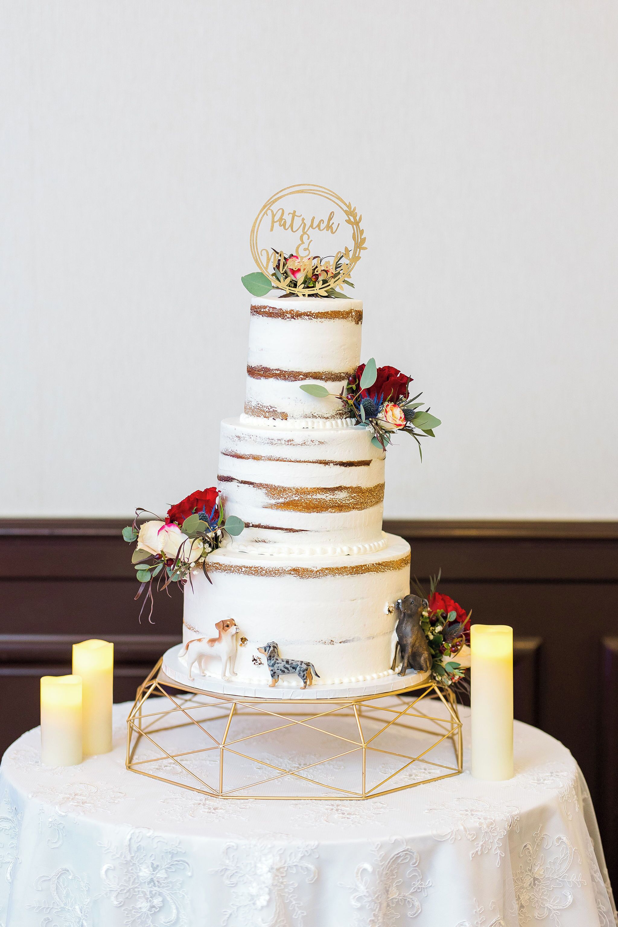 A multi-tiered wedding cake with a gold and white color scheme, adorned with flowers and a topper that reads "Patrick & Emily".
