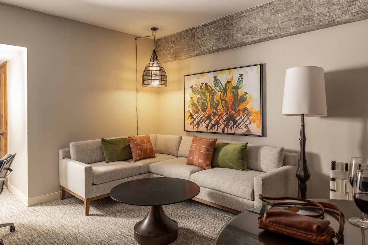 Un salon moderne avec un canapé d’angle, une table basse ronde, un luminaire suspendu, une lampe sur pied et un tableau au mur.