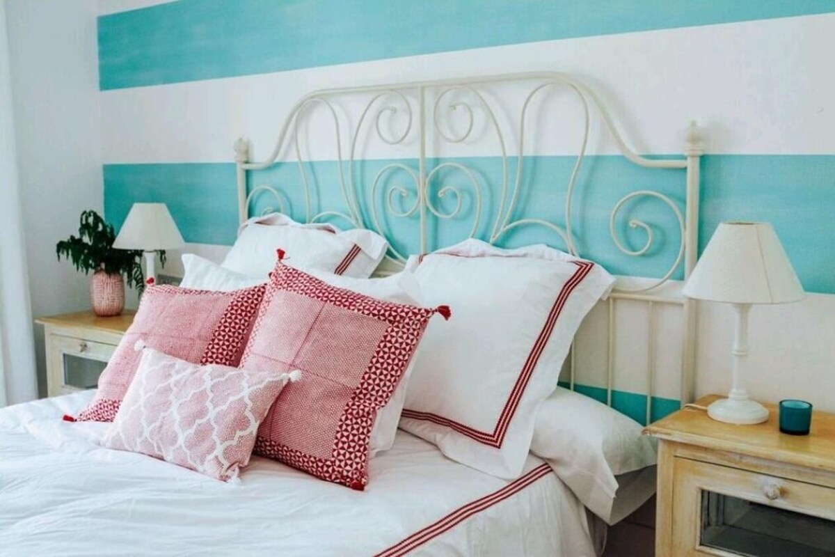 Una cama con ropa de cama blanca y almohadas decorativas, cabecera de metal blanco y mesitas de noche con lámparas.