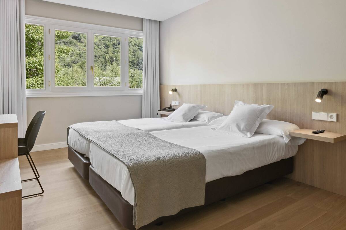 Una habitación de hotel moderna con una cama grande, un escritorio y una ventana con vistas a zonas verdes.