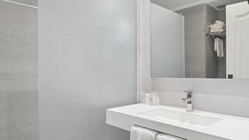 Un bagno moderno con un lavandino bianco, uno specchio e uno spazio doccia.