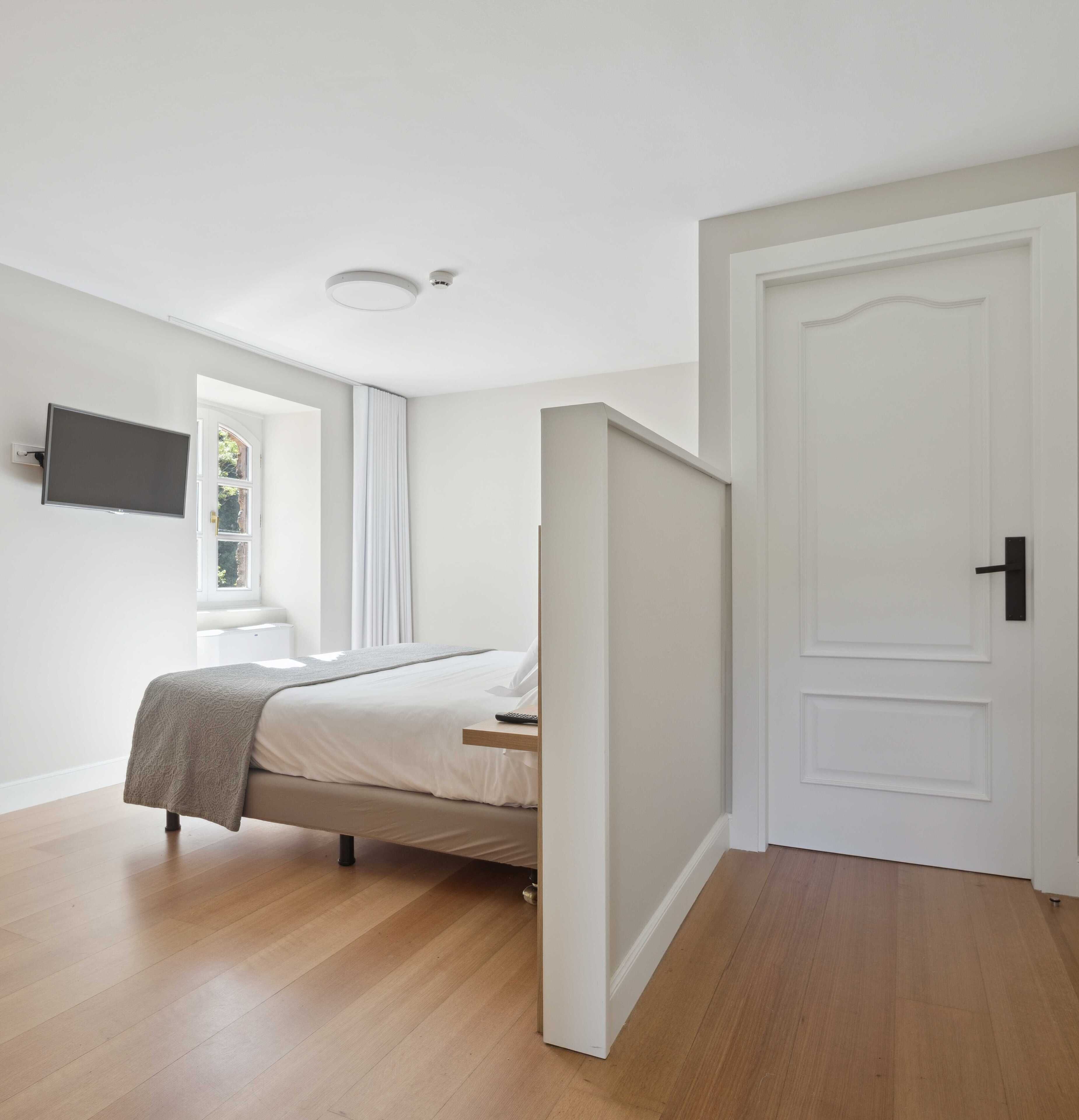 Una camera da letto moderna con un letto, una TV montata a parete e una porta che dà su un'altra stanza.