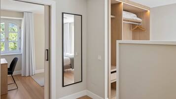 Ein modernes Zimmer mit Holzboden, einem großen Spiegel, einem Kleiderschrank mit Platz zum Aufhängen und einer Tür zu einem weiteren Zimmer.