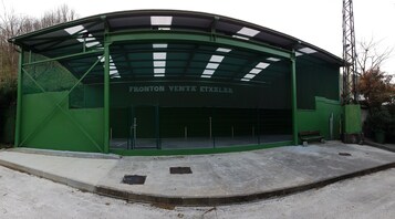 Un edificio verde con un vestíbulo cubierto y un letrero que dice "FRONTON VENTA ETXALAR".
