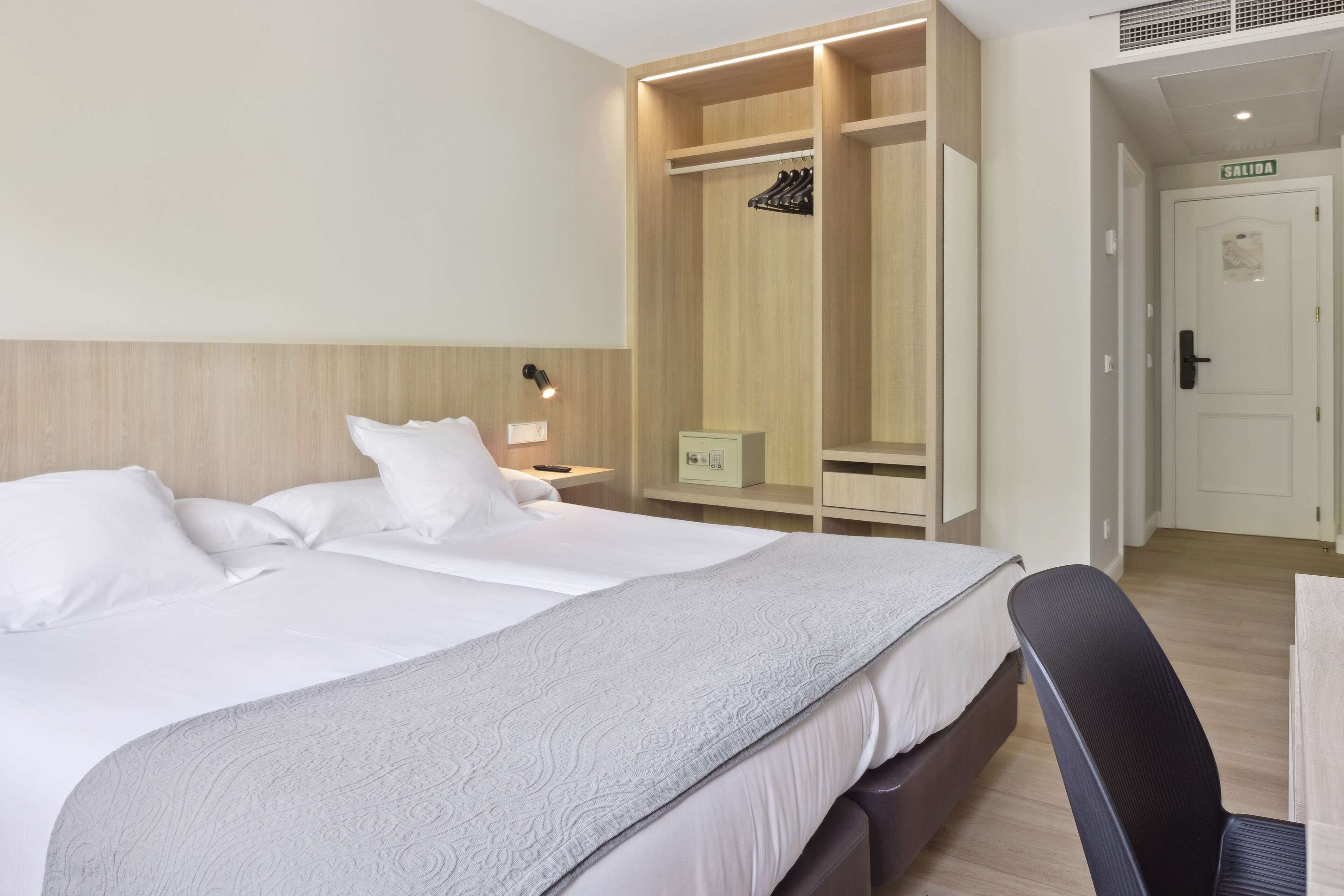 A hotel room with a large bed, a wardrobe, a desk, and a chair.