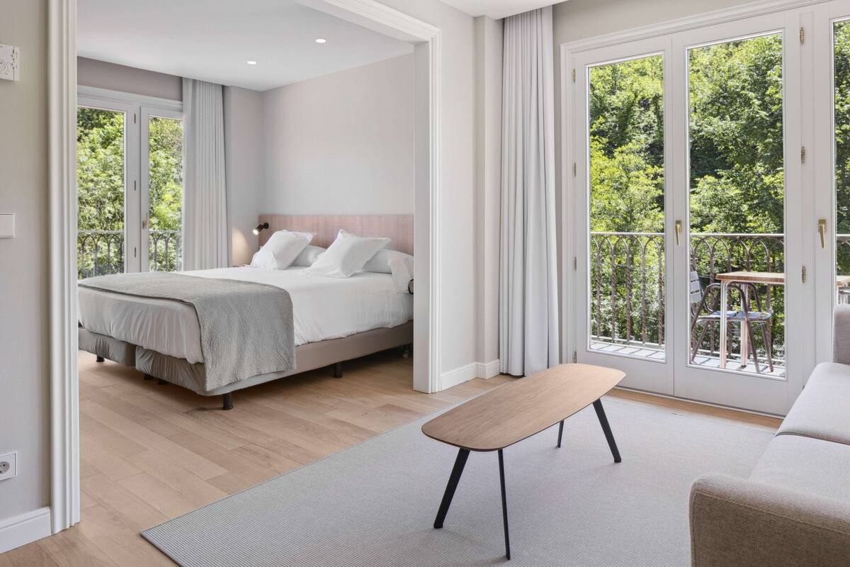 Habitación de hotel moderna con cama, una mesita y un balcón con vistas a zonas verdes.
