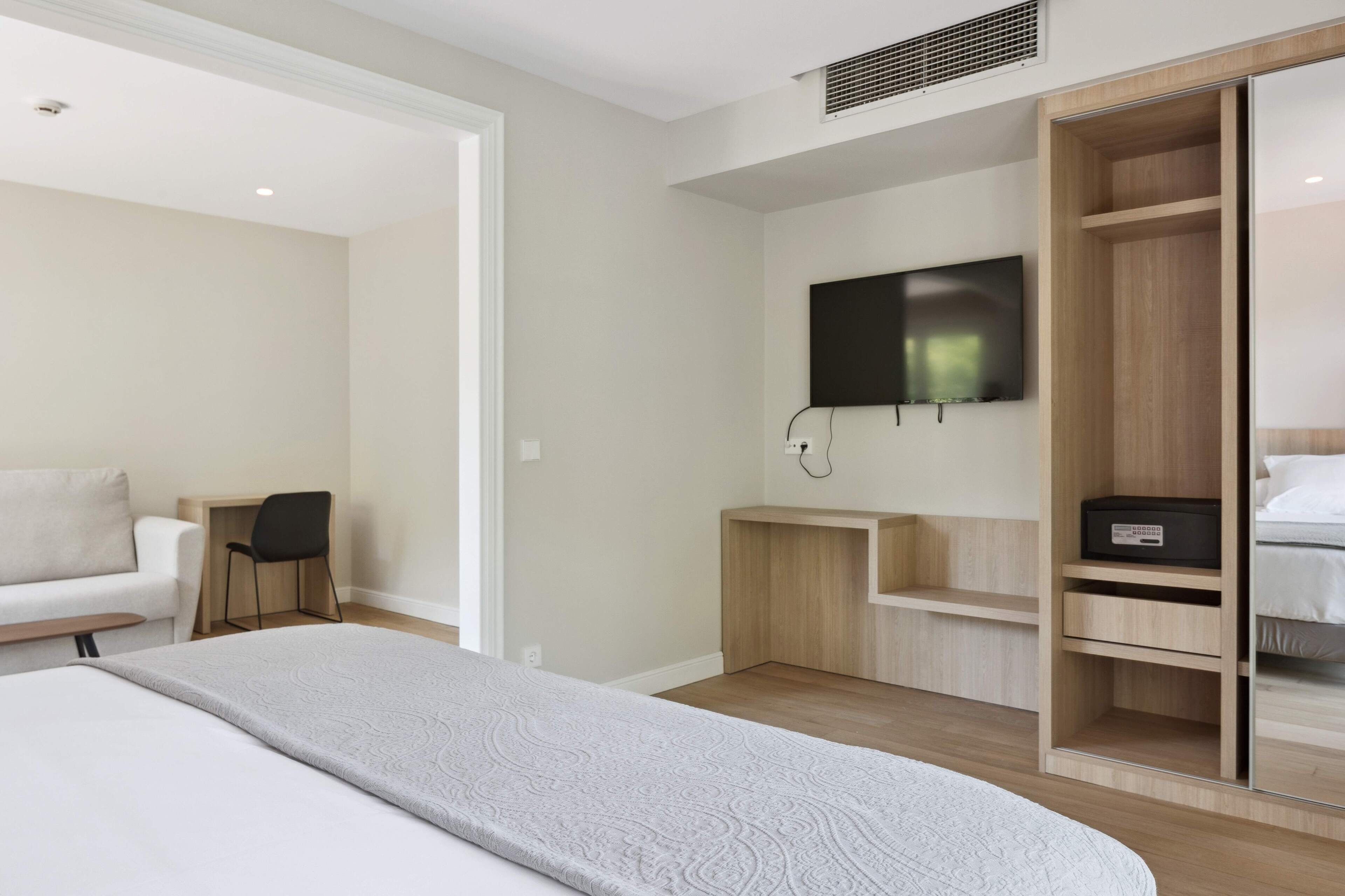 Una habitación de hotel moderna con una cama, un televisor montado en la pared, un armario de madera y un escritorio con una silla.