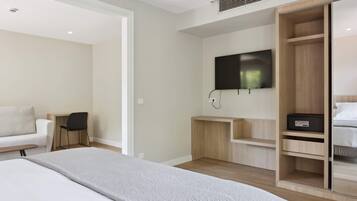 Una habitación de hotel moderna con una cama, un televisor montado en la pared, un armario de madera y un escritorio con una silla.