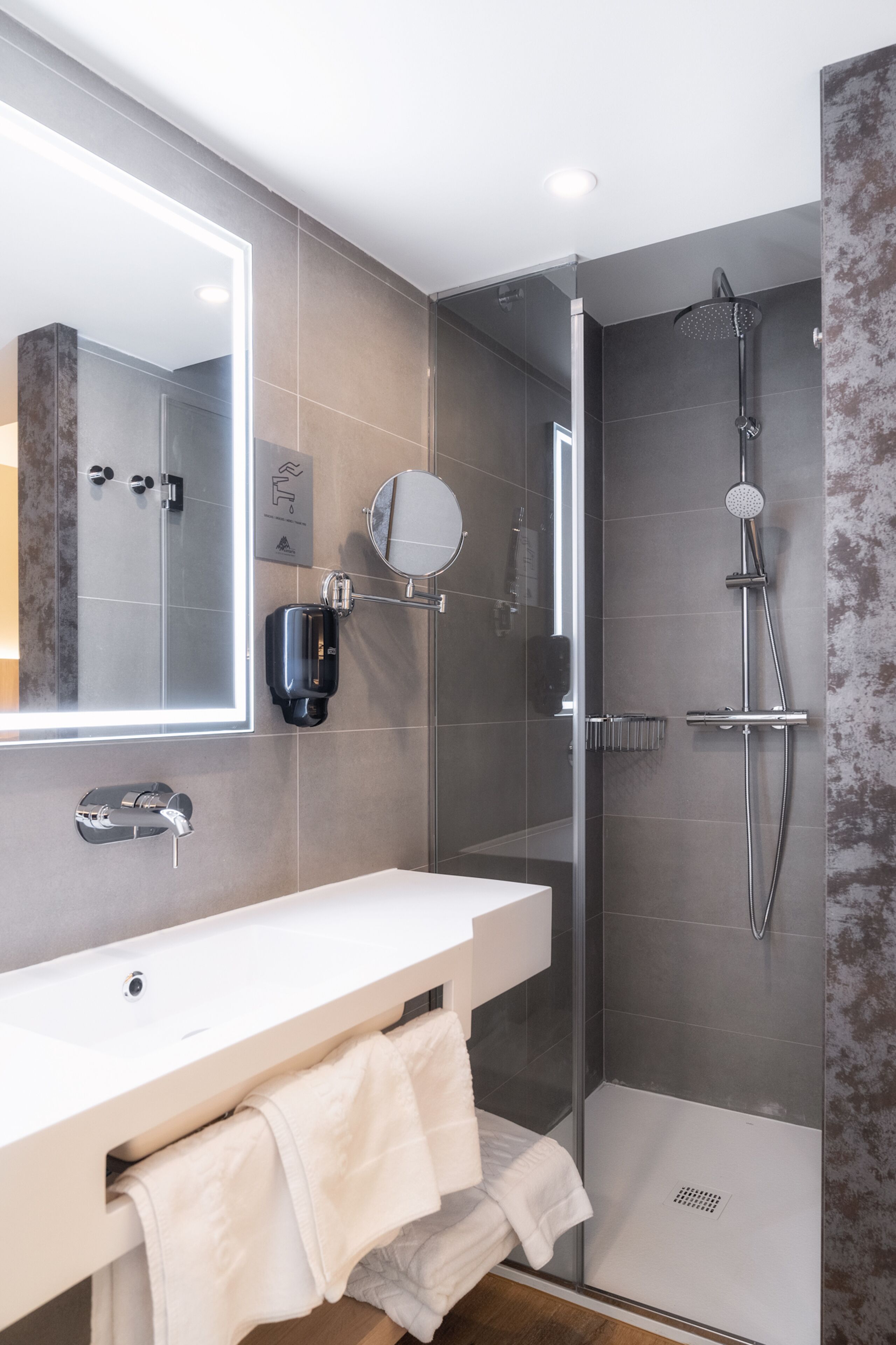 Un baño moderno con ducha envuelta en vidrio, lavabo blanco y un espejo grande.