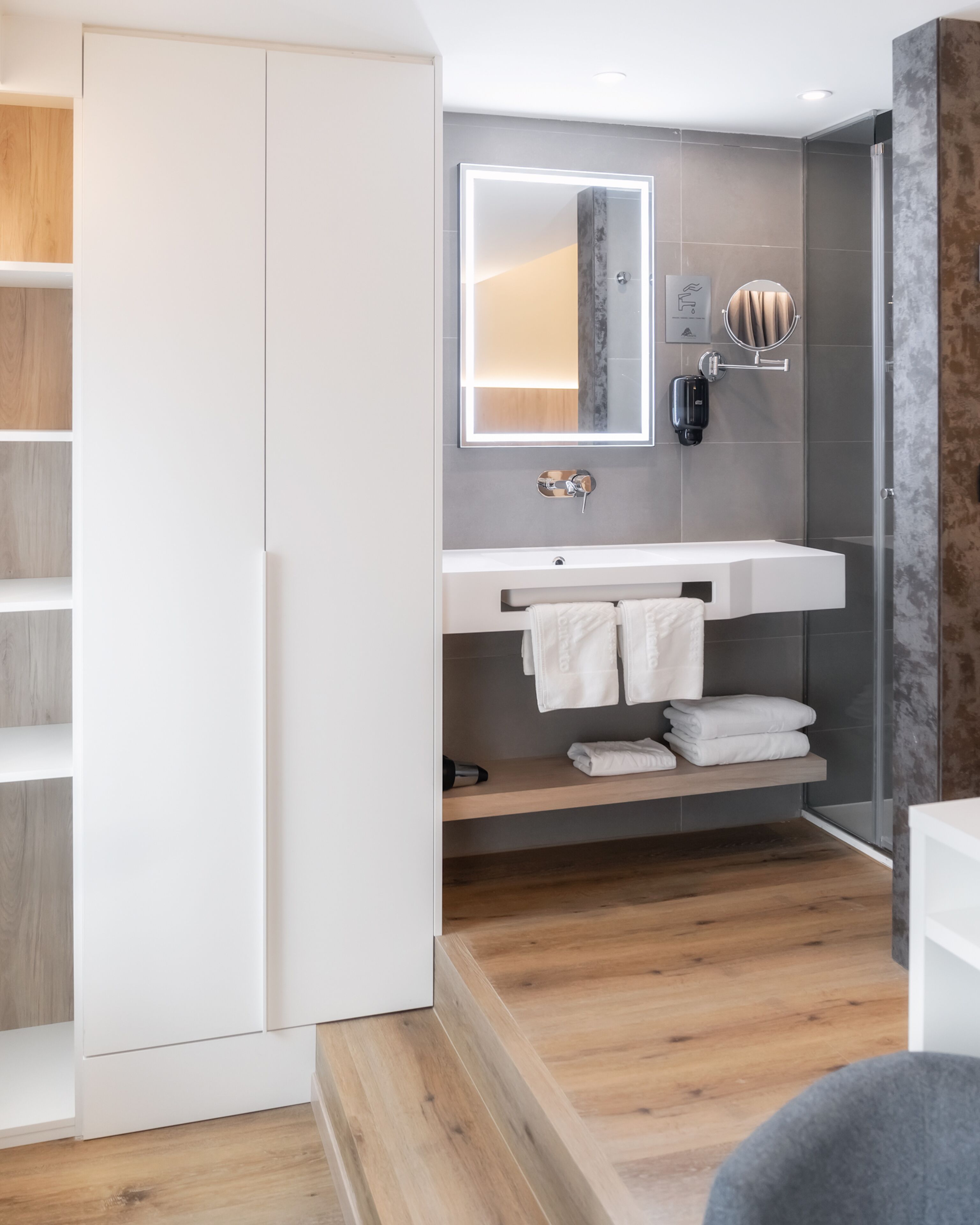 A modern bathroom with a white vanity, a glass shower enclosure, and a wooden floor.