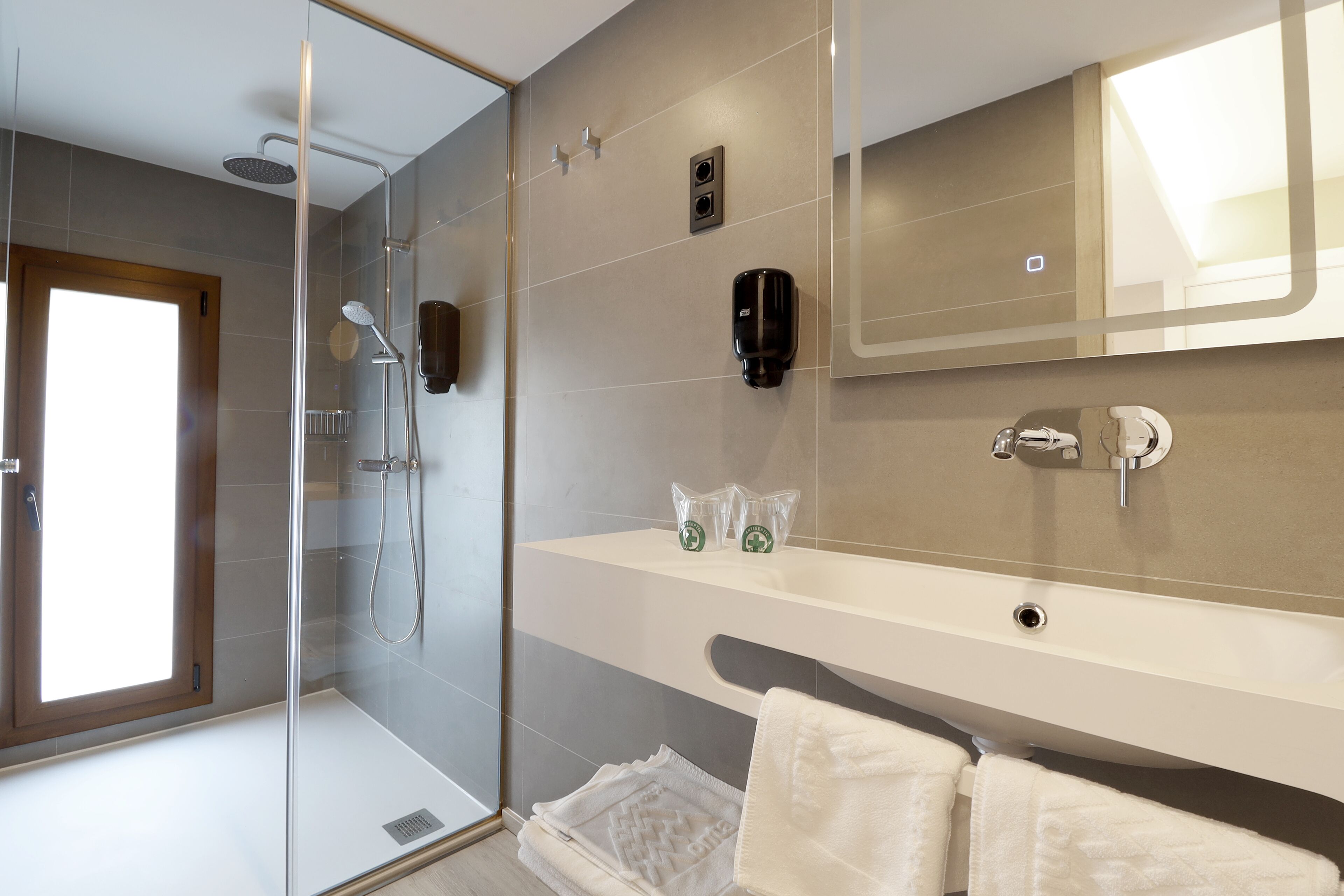 A modern bathroom with a glass-enclosed shower, a large mirror, and a white sink with a towel rack.