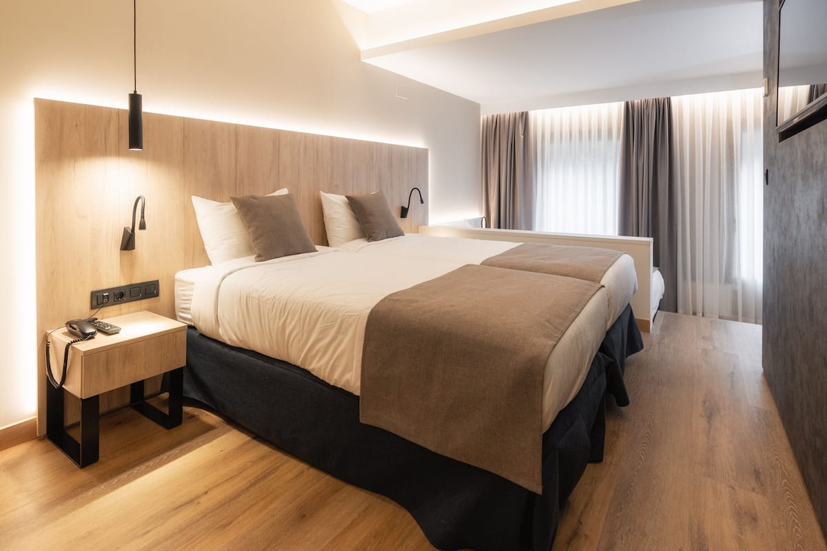 A modern hotel room with a large bed, bedside tables, a phone, and a lamp.