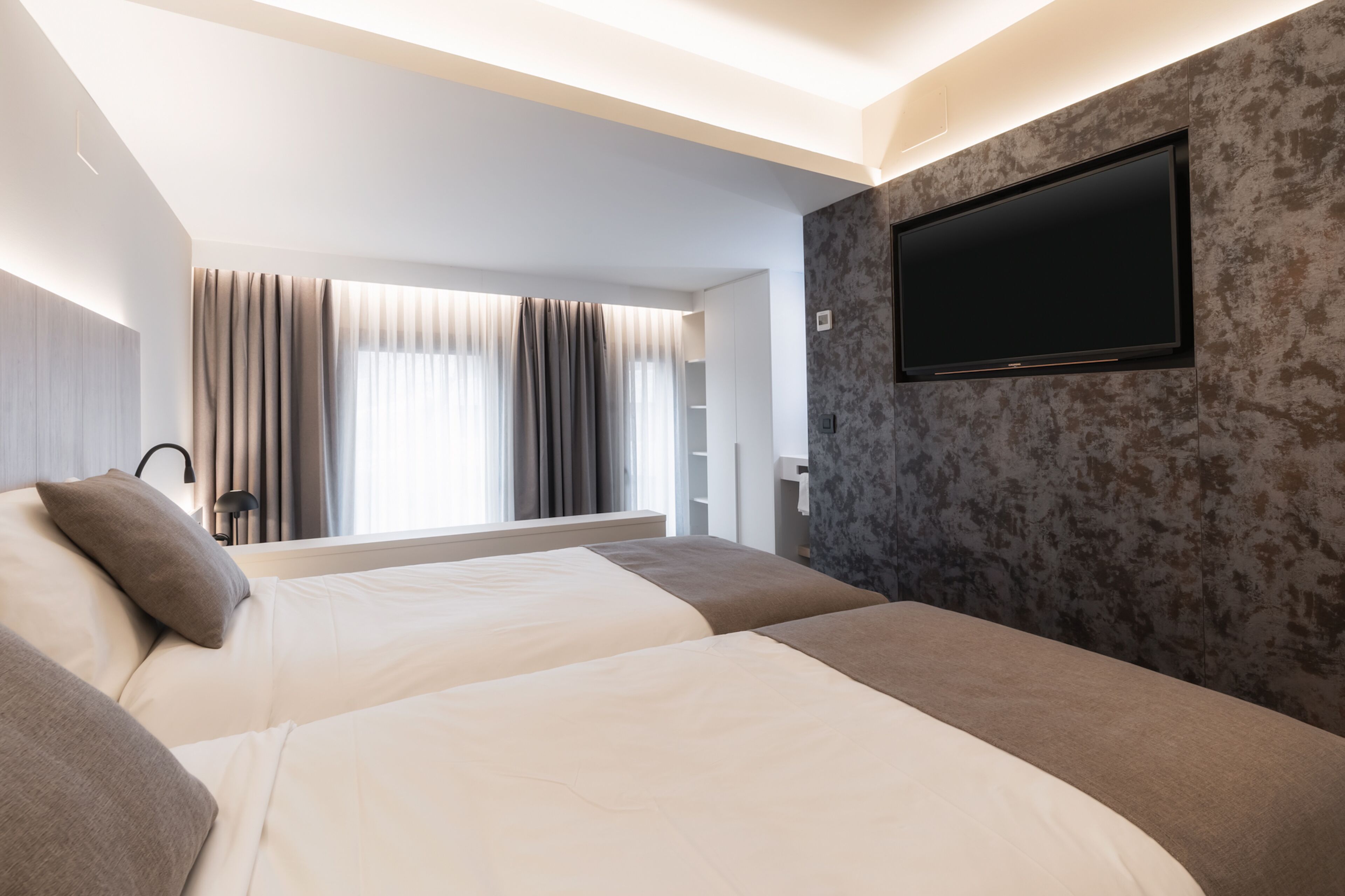 A modern hotel room with two beds, a flat-screen TV, and a large window with curtains.