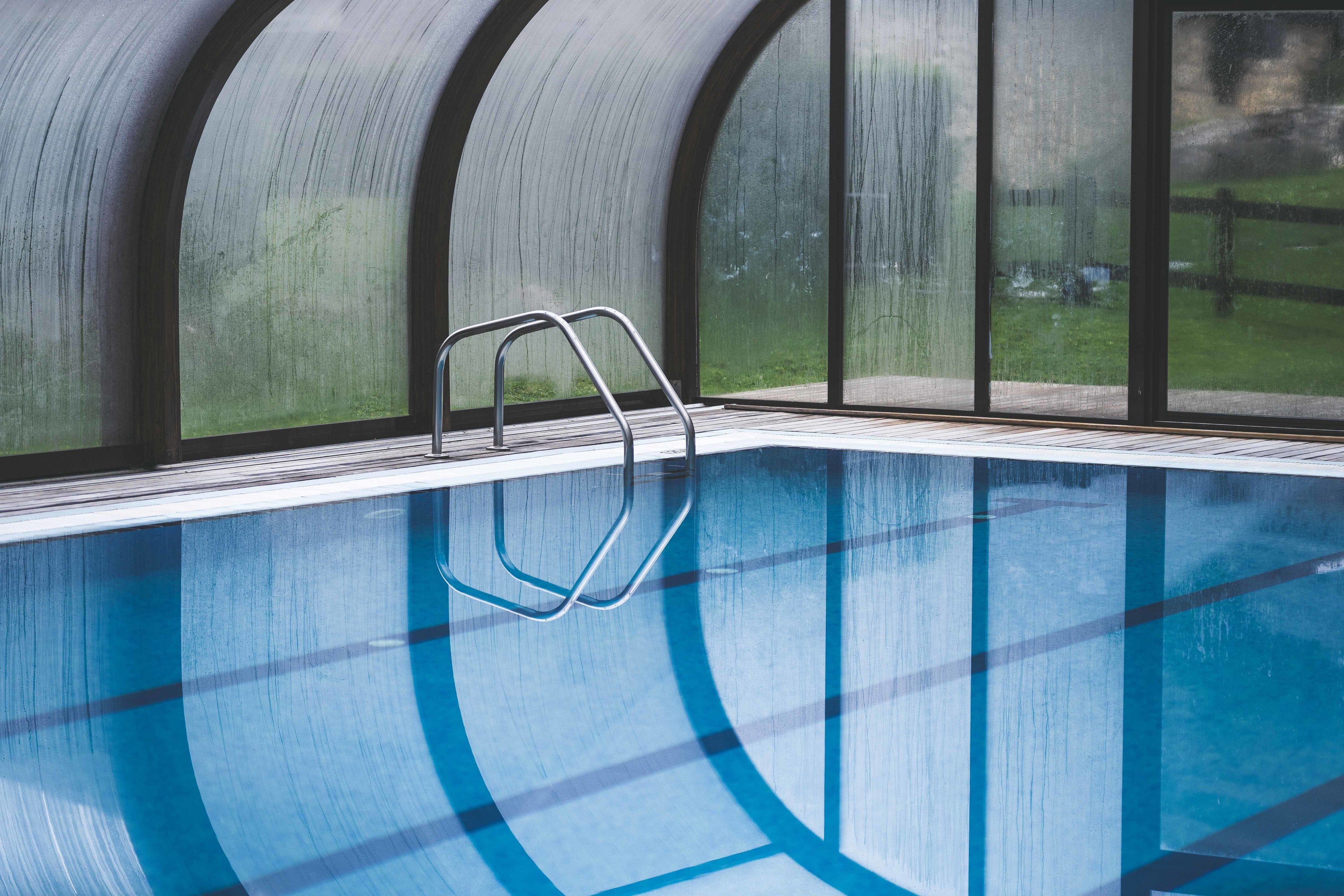 An indoor swimming pool with clear glass walls and a metal ladder.