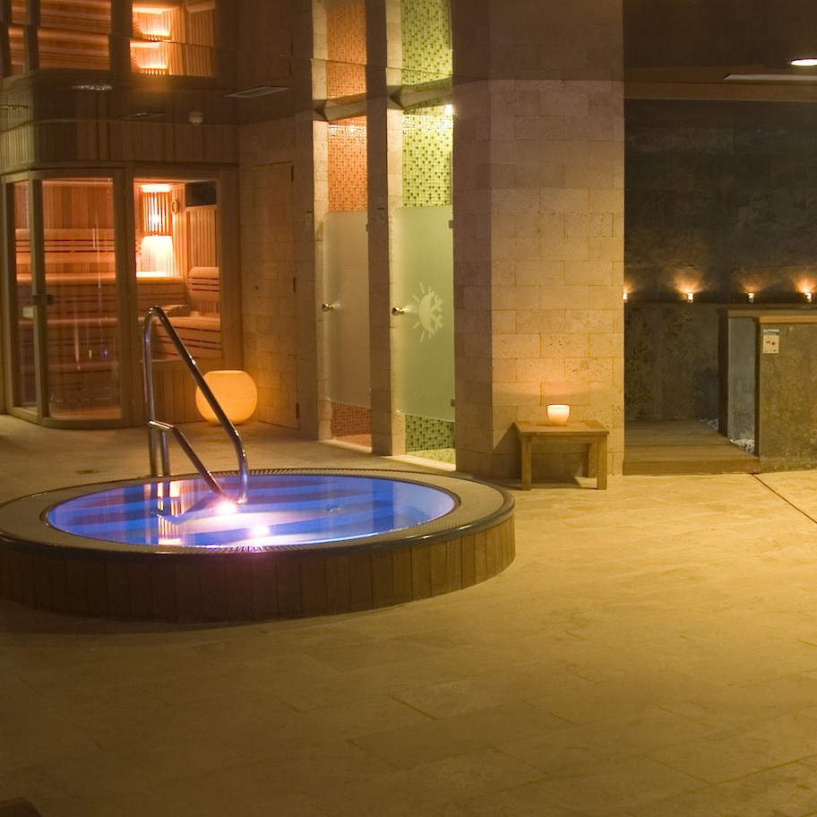 A spa area with two hot tubs, wooden benches, and a stone wall.
