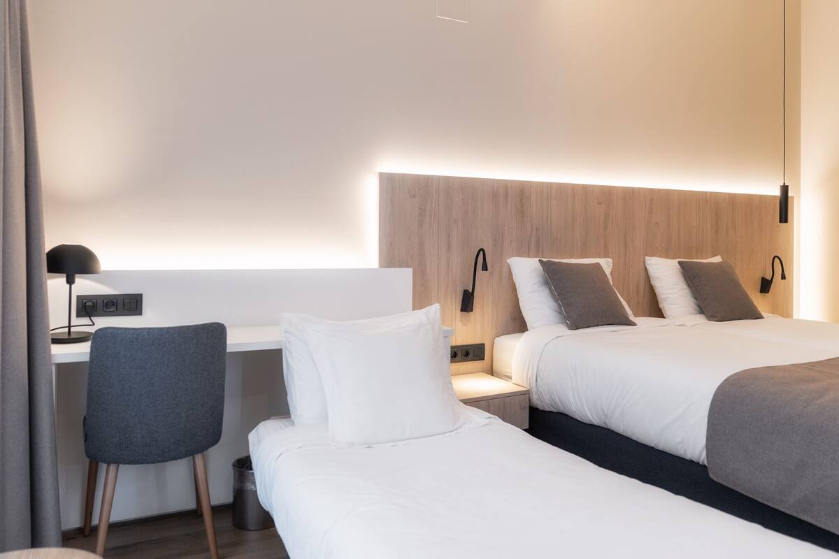 A hotel room with two beds, a desk, and a chair.