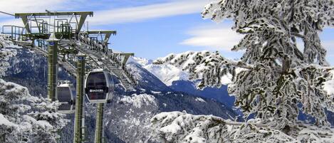 Um sistema de teleférico com uma cadeira de gôndola Baqueira, árvores cobertas de neve e montanhas ao fundo.
