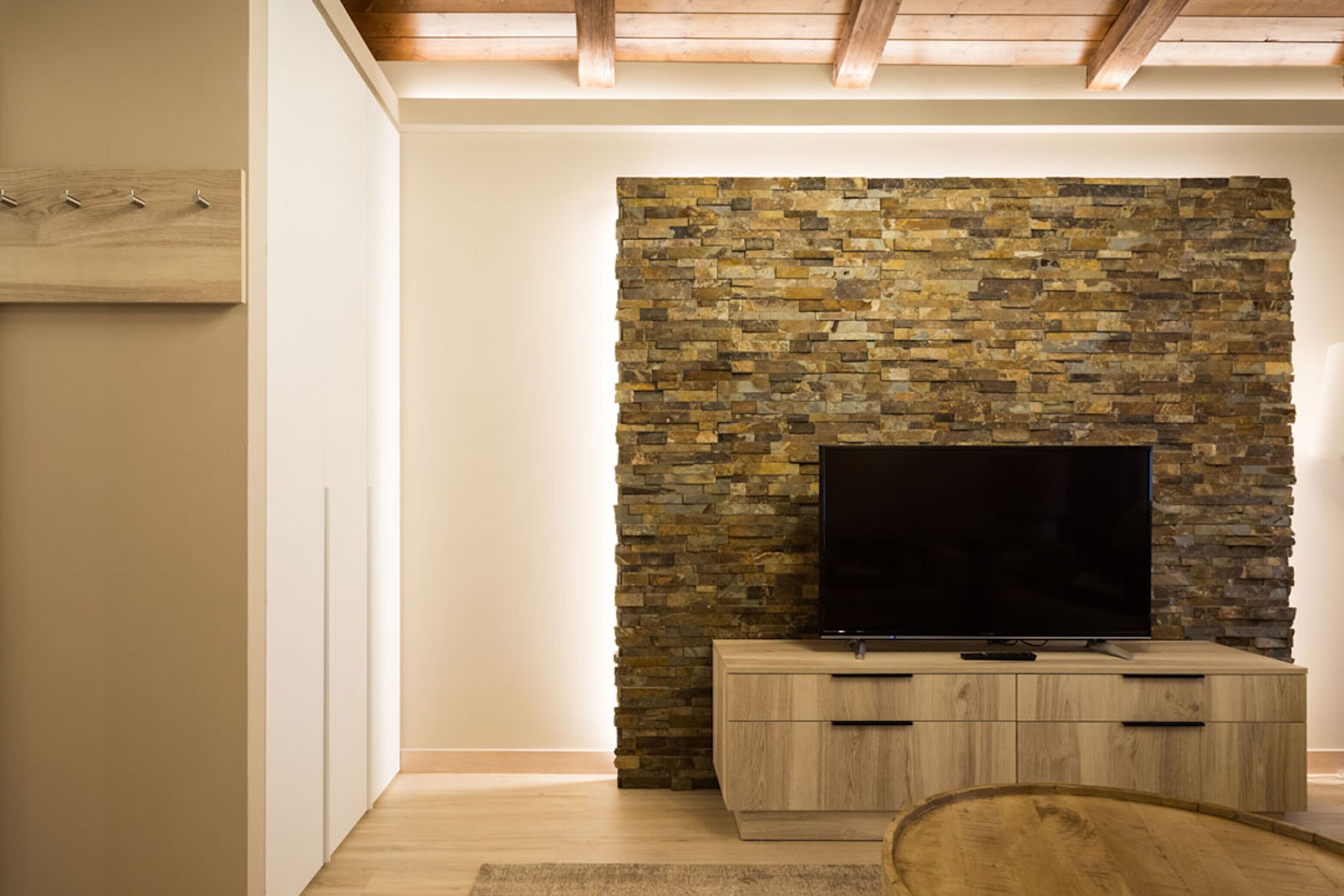 A modern living room with a stone wall, wooden entertainment unit, and a flat-screen TV.