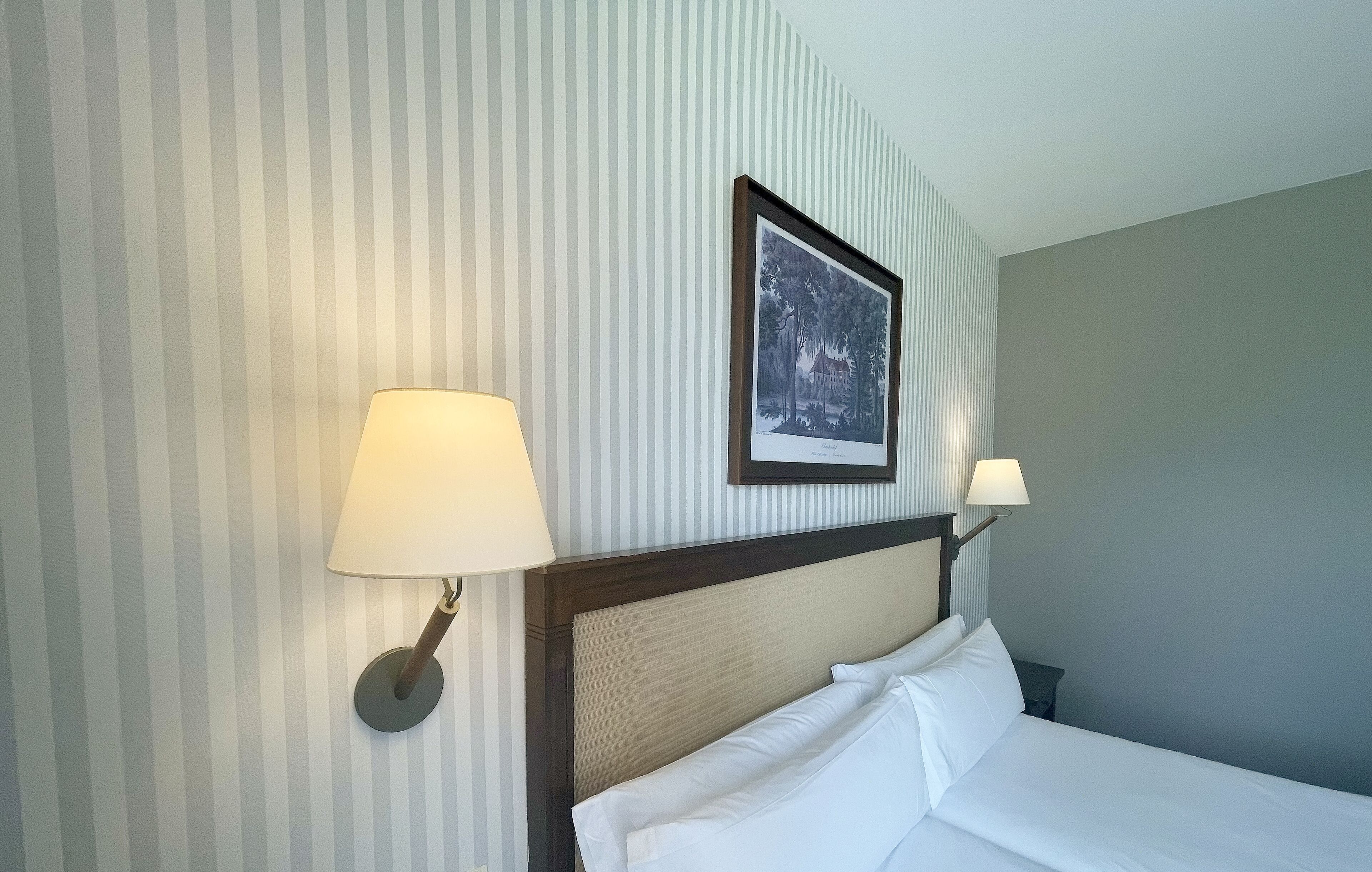 A hotel room with striped wallpaper, a framed picture on the wall, and two bedside lamps.