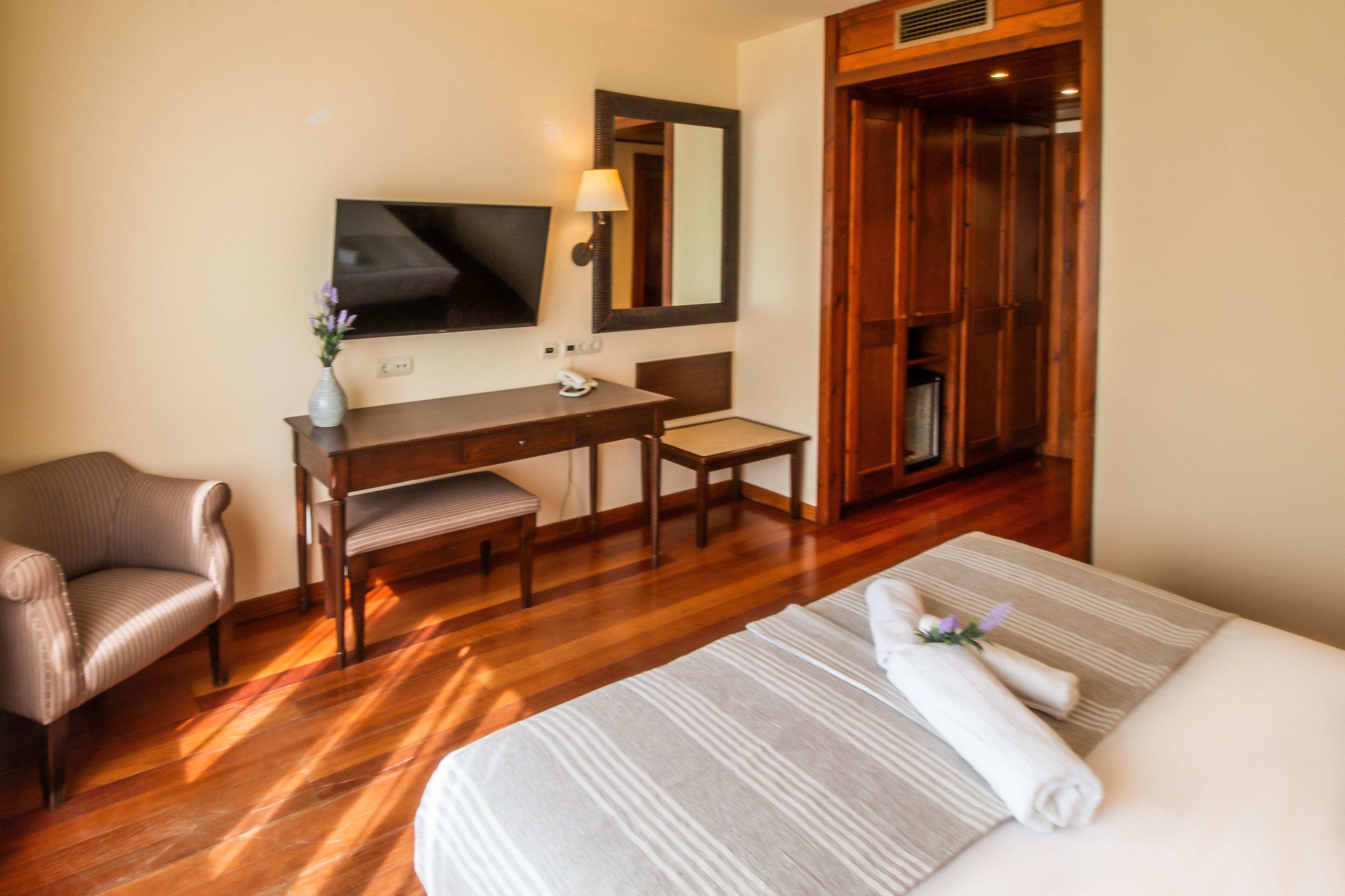 A hotel room with a bed, a desk, a chair, a television, and a mirror.